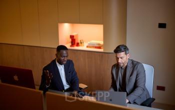 Two professionals engage in a business meeting at Zeestraat 70, The Hague Center. The office features modern decor with built-in shelving, offering a practical space for office space rental.