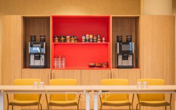 Modern office pantry at Zeestraat 70, The Hague Center with sleek wooden cabinets, vibrant red accents, and coffee machines, perfect for office space rental convenience.