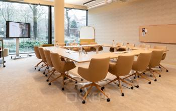 Spacious and modern conference room at Zeestraat 70, The Hague Center, featuring a large wooden table, comfortable swivel chairs, and a presentation screen, ideal for office space rental.