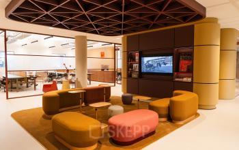 Modern office interior at Zeestraat 70, The Hague Center, featuring cozy lounge area with colorful seating, adjacent to glass-enclosed workspace, suitable for office space rental.