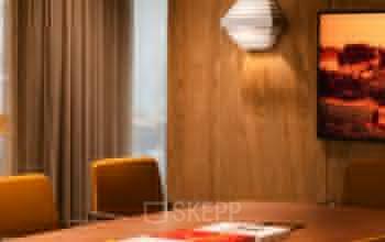 Warm and inviting conference room at Zeestraat 70 in The Hague Center, featuring stylish wooden walls, a modern light fixture, and a large table with books and a bowl of lemons. Office space rental available.