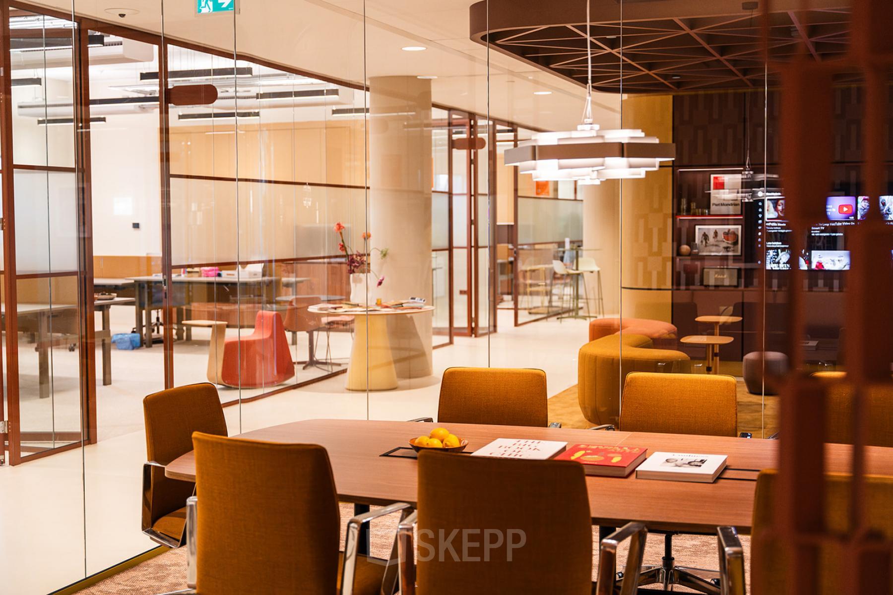 Modern conference room at Zeestraat 70 in The Hague Center, featuring stylish orange chairs around a large table, accented by contemporary lighting and a glass partition. Ideal for office space rental.