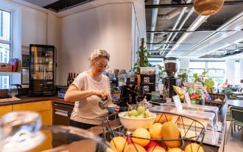 Woman preparing a beverage in a well-lit office lounge area at Fluwelen Burgwal 58, highlighting office space rental opportunities in The Hague Center.