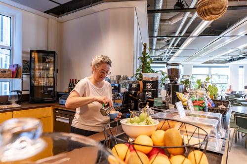 Woman preparing a beverage in a well-lit office lounge area at Fluwelen Burgwal 58, highlighting office space rental opportunities in The Hague Center.