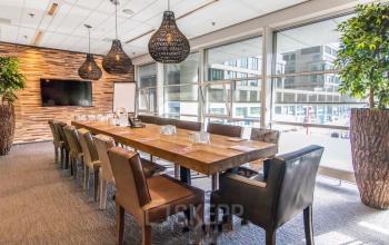 Conference room at Kalvermarkt 53, The Hague Center, featuring a large wooden table, leather chairs, modern lighting, and large windows offering natural light. Office space rental in a professional setting.