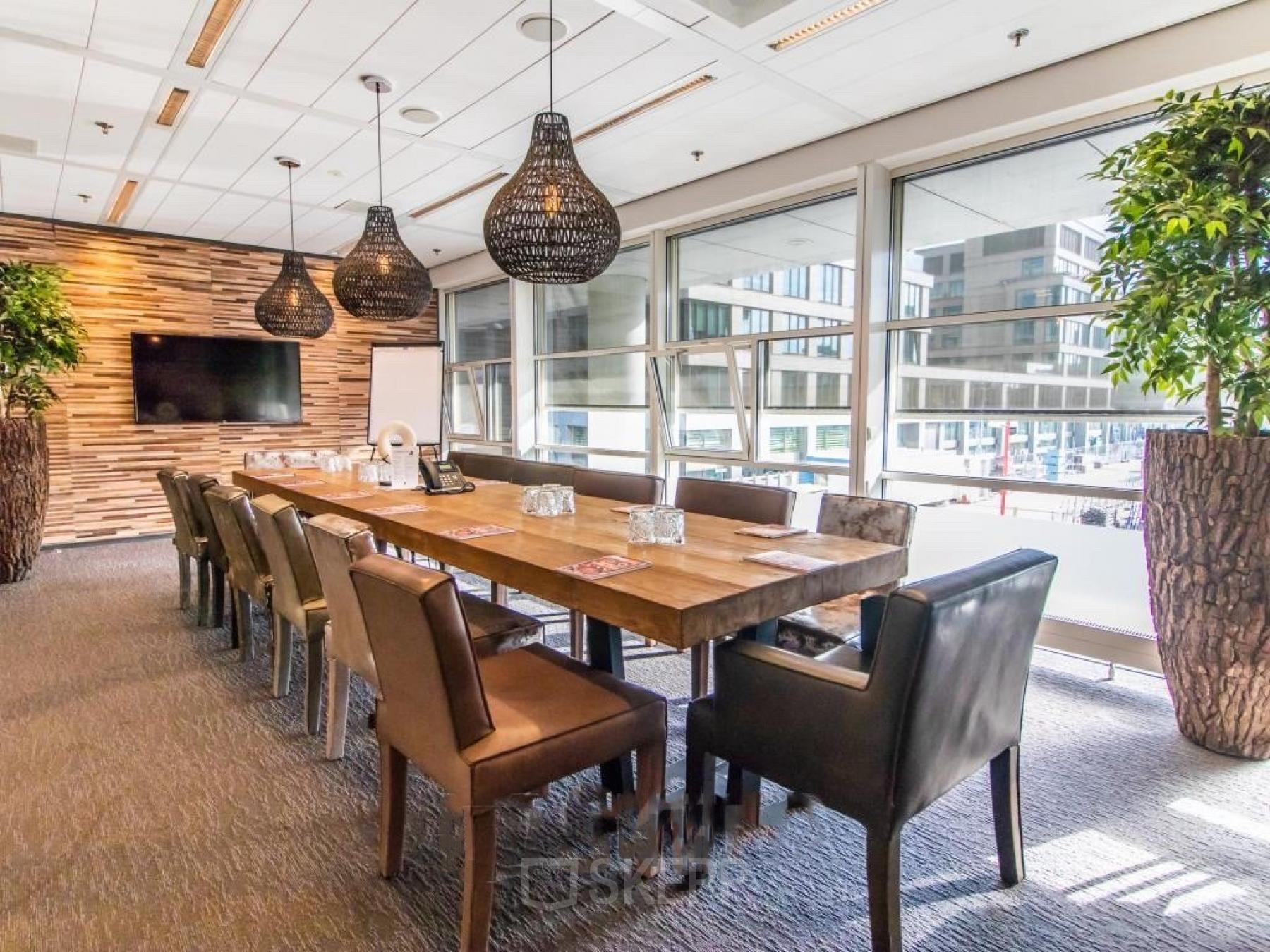 Conference room at Kalvermarkt 53, The Hague Center, featuring a large wooden table, leather chairs, modern lighting, and large windows offering natural light. Office space rental in a professional setting.