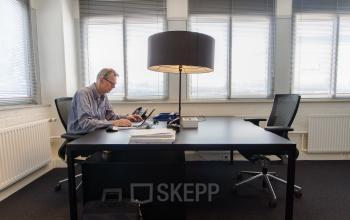 A professional working at a desk in a bright, furnished office at Platinaweg 25, The Hague Escamp, ideal for office space rental.