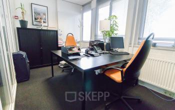 Furnished office at Platinaweg 25, The Hague Escamp available for rent, features two orange office chairs, a black desk with computers, and ample natural light from large windows.