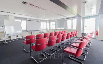Bright office space with rows of red chairs facing a whiteboard and projector screen, ideal for conferences or presentations at Platinaweg 25, The Hague Escamp, perfect for office space rental.