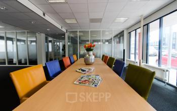 Bright meeting room at Platinaweg 25, The Hague Escamp, perfect for office space rental. Vibrant chairs surround a long table with magazines and a flower vase.
