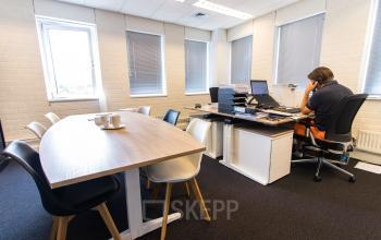 Office space at Platinaweg 25, The Hague Escamp, featuring a person working at a desk with a phone and computer, alongside a meeting table with chairs.
