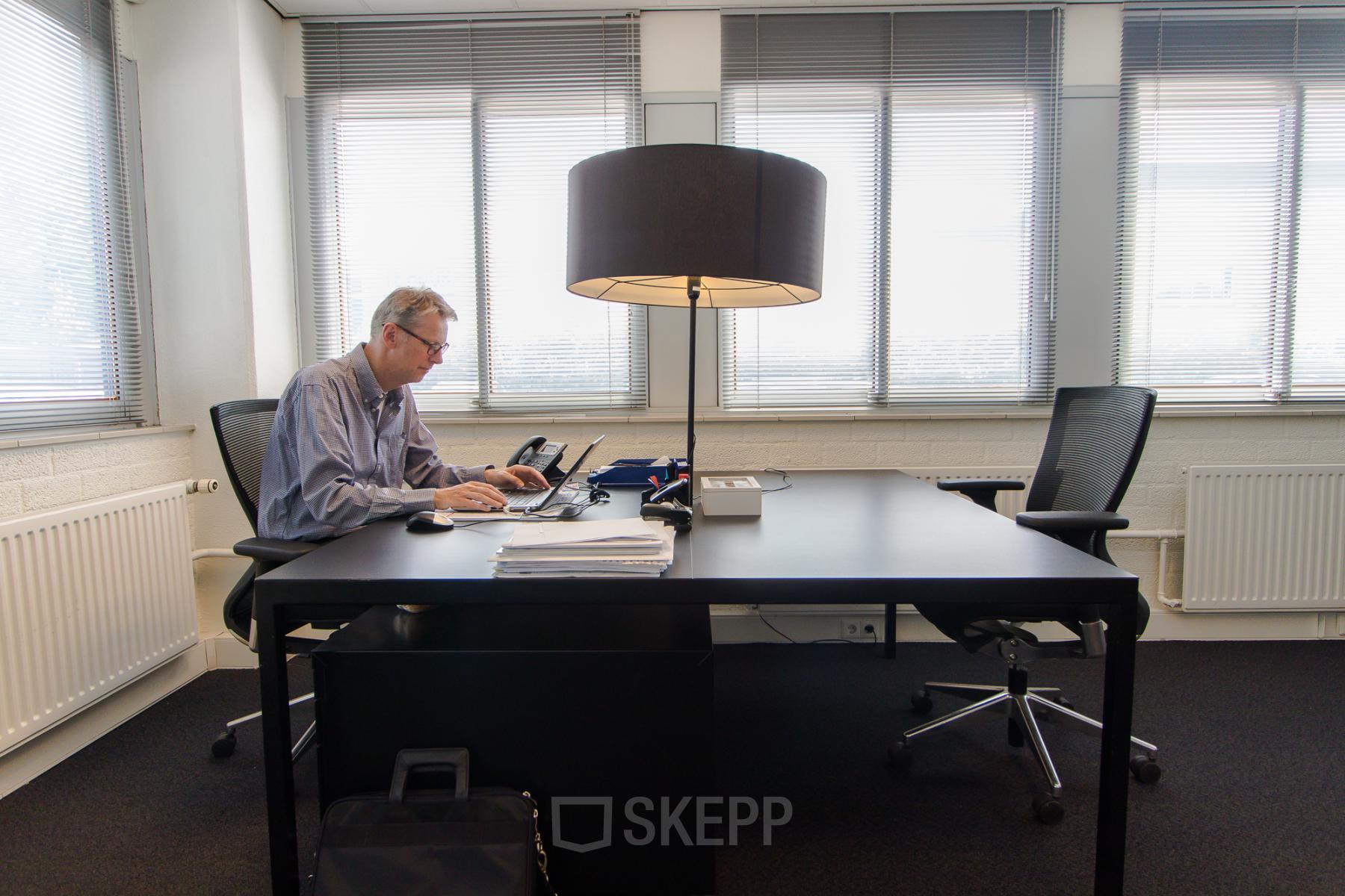 A professional working at a desk in a bright, furnished office at Platinaweg 25, The Hague Escamp, ideal for office space rental.
