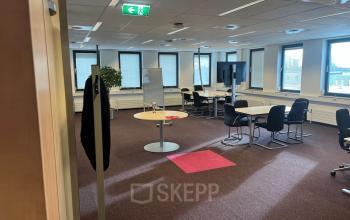 Spacious office featuring workstations, chairs, and a whiteboard, ideal for office space rental. Located at Platinaweg 10 in The Hague Escamp. Natural light fills the workspaces.