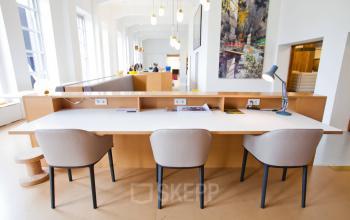 Modern and well-lit office space rental at Zuid Hollandlaan 7, The Hague Haagse Hout, featuring a large communal desk with stylish chairs and pendant lighting.