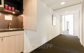 Bright office hallway with a small kitchenette featuring wooden cabinets and a sink, located at Bezuidenhoutseweg 161 in The Hague Haagse Hout, available for office space rental.