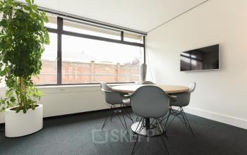 Furnished office space with a round meeting table, chairs, a large window, and a wall-mounted TV at Bezuidenhoutseweg 161 in The Hague Haagse Hout, ideal for office space rental.