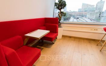 Bright office space rental at Jan Pietersz. Coenstraat 7, The Hague Haagse Hout, featuring a vibrant red couch, wooden floors, and a city view.