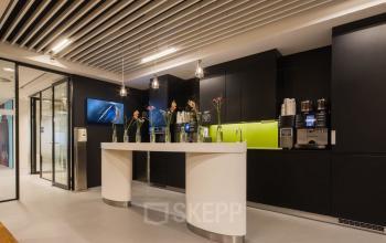 Modern office with sleek design at Prinses Margrietplantsoen 25, The Hague, featuring a stylish pantry area with black cabinets, a vibrant green backsplash, and a coffee station ideal for office space rental.