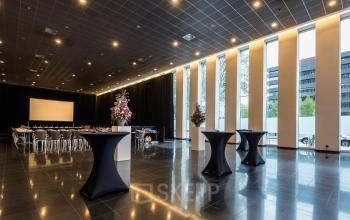 Spacious conference room at Prinses Margrietplantsoen 25, The Hague Haagse Hout, featuring sleek black flooring, tall windows allowing natural light, and tables setup for events. Ideal for office space rental.