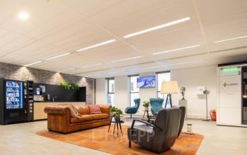Modern office lounge at Prinses Margrietplantsoen 25, The Hague Haagse Hout with comfortable seating, a vending machine, and TV. Ideal space for rent in a welcoming business environment.
