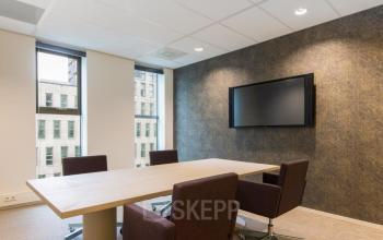 Modern conference room at Prinses Margrietplantsoen 25, The Hague Haagse Hout, featuring a wooden table, brown chairs, and a wall-mounted TV, perfect for office space rental.