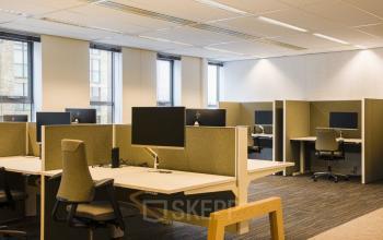 Modern office interior with multiple workstations at Prinses Margrietplantsoen 25, The Hague. The space is well-lit with large windows, contemporary furniture, and ample desk space, available for office space rental.