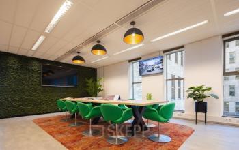 Modern conference room at Prinses Margrietplantsoen 25, The Hague, featuring a large table, green chairs, and a moss wall, ideal for office space rental. Ample natural light enhances the contemporary ambiance.