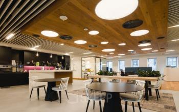 Modern furnished workspace with round tables, chairs, and a stylish ceiling in a The Hague office space rental location.