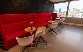 Modern office lounge at Schenkkade 50, The Hague Haagse Hout, featuring red bench seating and sleek tables with city views, available for office space rental.
