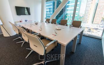 Modern conference room at Schenkkade 50 in The Hague Haagse Hout, ideal for office space rental, featuring a long table, several chairs, and a wall-mounted screen with a city view.