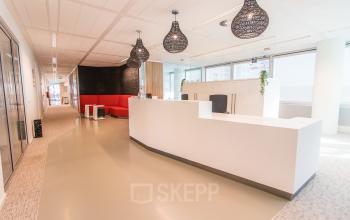 Bright and modern office space at Schenkkade 50, The Hague Haagse Hout, featuring a sleek white reception area with stylish lighting and a red seating area, available for office space rental.