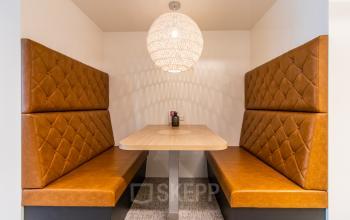 Cozy furnished booth setup in an office space rental at Schenkkade 50, The Hague Haagse Hout, featuring a wooden table between two brown cushioned benches.