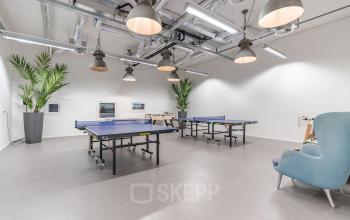 Modern office space rental at Oude Middenweg 3-19 in The Hague, with a recreation area featuring ping pong tables, stylish seating and bright lighting.
