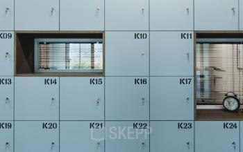 Locker wall with blue numbered compartments and a clock on a shelf, located at Oude Middenweg 3-19, The Hague Leidschenveen-Ypenburg.