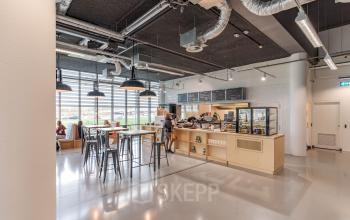 Spacious and well-lit office space rental at Oude Middenweg 3-19, The Hague, with a modern pantry area and individuals engaged in casual conversations.