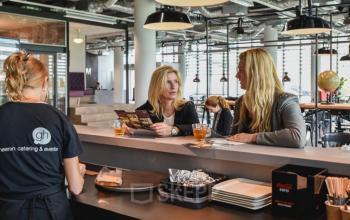 Professionals discuss business over coffee in a well-lit lounge area at Oude Middenweg 3-19 The Hague, perfect for office space rental.