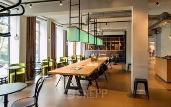 Modern office space rental at President Kennedylaan 19, The Hague, with green chairs, large wooden tables, and stylish lighting fixtures.