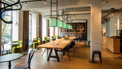 Modern office space rental at President Kennedylaan 19, The Hague, with green chairs, large wooden tables, and stylish lighting fixtures.