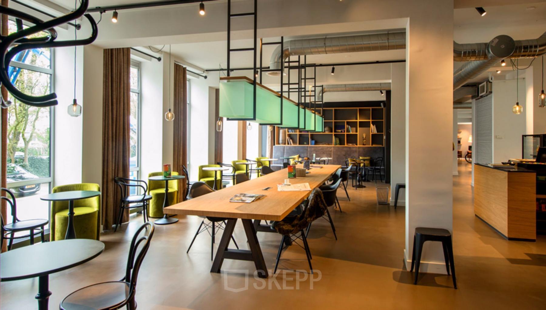 Modern office space rental at President Kennedylaan 19, The Hague, with green chairs, large wooden tables, and stylish lighting fixtures.