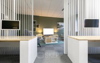 Modern workspace in an office to rent at Keulenstraat 12, Deventer, featuring wooden desks, white dividers, and a cozy seating area with a TV and bookshelf.