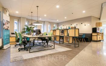 Modern workspace with green chairs, desks, and shelf units at Keulenstraat 12, Deventer. Bright lighting and plants enhance the office space rental atmosphere.