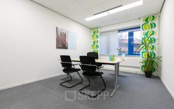 Office space rental at Keulenstraat 12, Deventer, featuring a meeting table with chairs, whiteboard, large window, and colorful wall art.