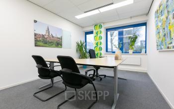 Office space rental at Keulenstraat 12, Deventer, featuring a meeting table with chairs, wall art, and plants by the window.