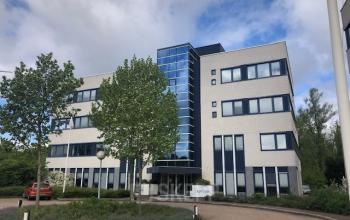 Exterior view of the office building at Keulenstraat 15, Deventer. This modern structure offers office space rental opportunities in a professional neighborhood, surrounded by lush greenery and ample parking space for convenience.