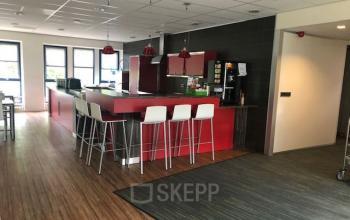 A modern office pantry with a red counter and high white chairs at Keulenstraat 15, Deventer. Ideal for office space rental, the room features sleek wooden flooring and contemporary lighting.