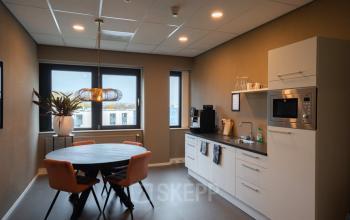 Modern office kitchen area at Keulenstraat 1, Deventer, available for office space rental, featuring a round table with chairs, microwave, and coffee machine.