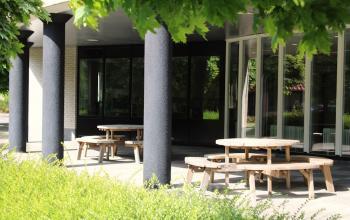 Exterior view of office building at Keulenstraat 12, Deventer, featuring outdoor seating area with round wooden tables and benches.