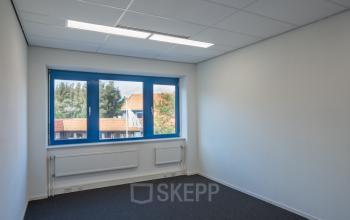 Empty office space with grey carpet and large blue-framed window at Keulenstraat 12, Deventer - ideal for office space rental.