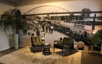 Office space rental at Keulenstraat 12, Deventer featuring a cozy lounge area with two chairs, a small table, and a large wall mural depicting a historical scene.