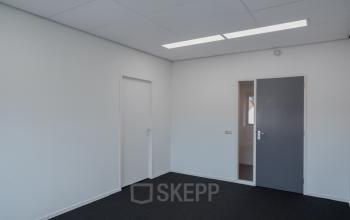 Office space with simple white walls and dark carpeting located at Keulenstraat 12, Deventer. One door leads to a hallway.